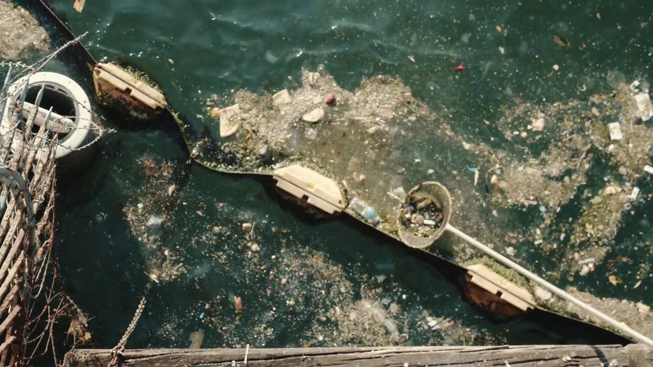 环境污染的概念。从上往下看，许多塑料垃圾漂浮在肮脏的海水中，人们用网把它捞出来。视频素材