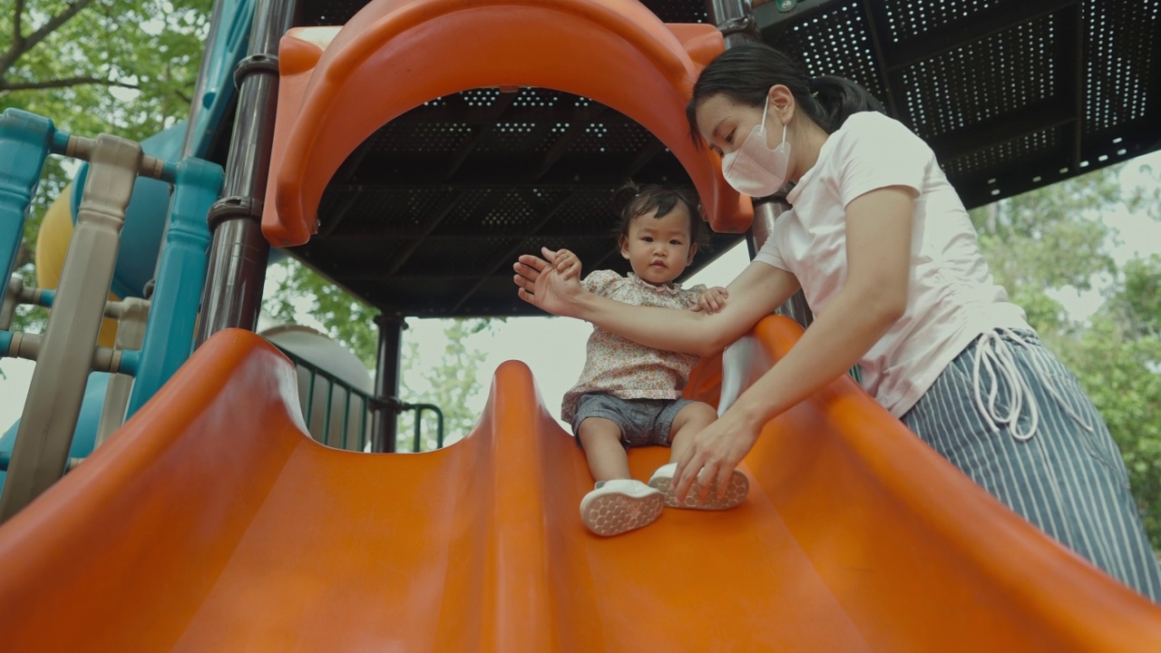 积极情绪亚洲母亲抱着女儿在公共游乐场玩滑梯在公共公园的家庭生活视频素材
