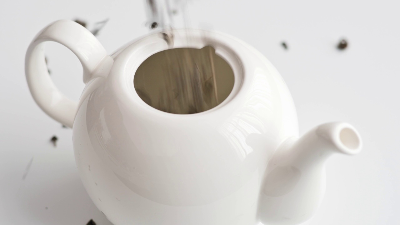 干茶叶倒进白色的陶瓷茶壶在白色的桌子上。泡茶的概念。古典茶道。把绿茶，红茶，花草茶放在茶壶里。健康的生活方式视频下载