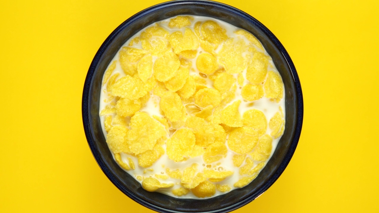 金黄色的玉米片，牛奶在黄色的背景上旋转。俯视图视频下载