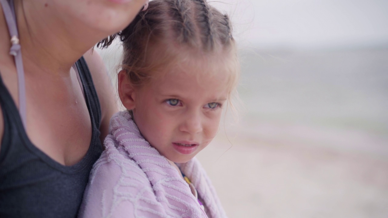 母亲拥抱着温暖的小女儿，把毛巾擦到户外阳光明媚的沙滩上视频素材
