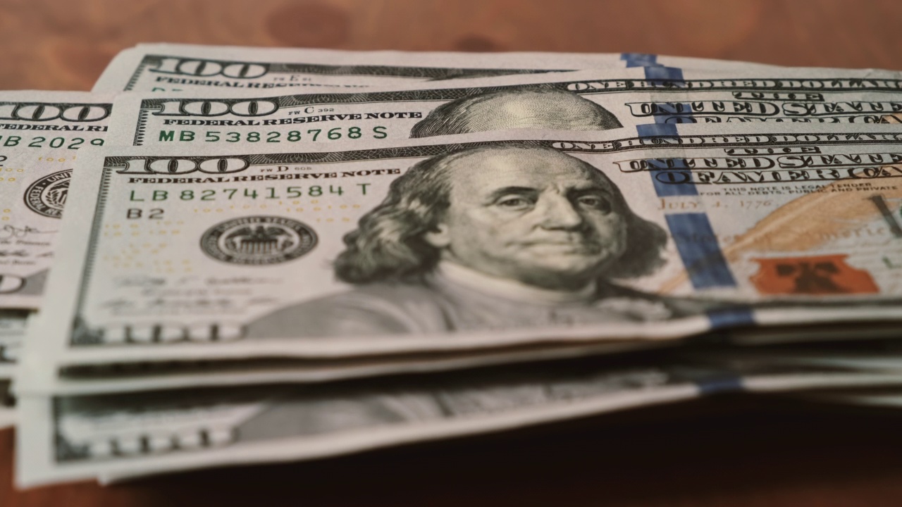 一百美元的钞票在木桌上一张接一张地增加。视频下载