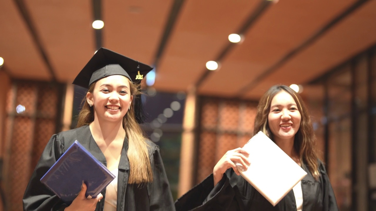 亚洲十几岁的女孩穿着毕业礼服布带着心情开心。穿黑色毕业礼服的人持有毕业证书。视频素材