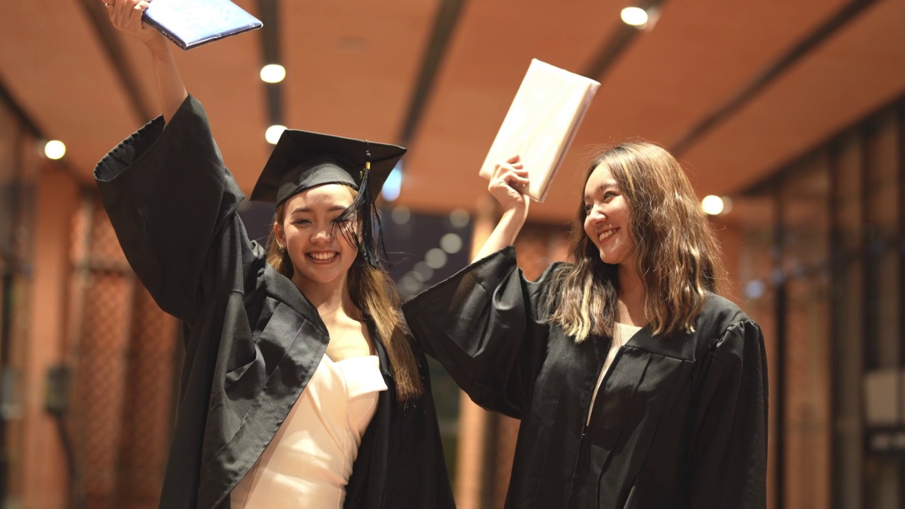 亚洲十几岁的女孩穿着毕业礼服布带着心情开心。穿黑色毕业礼服的人持有毕业证书。视频素材