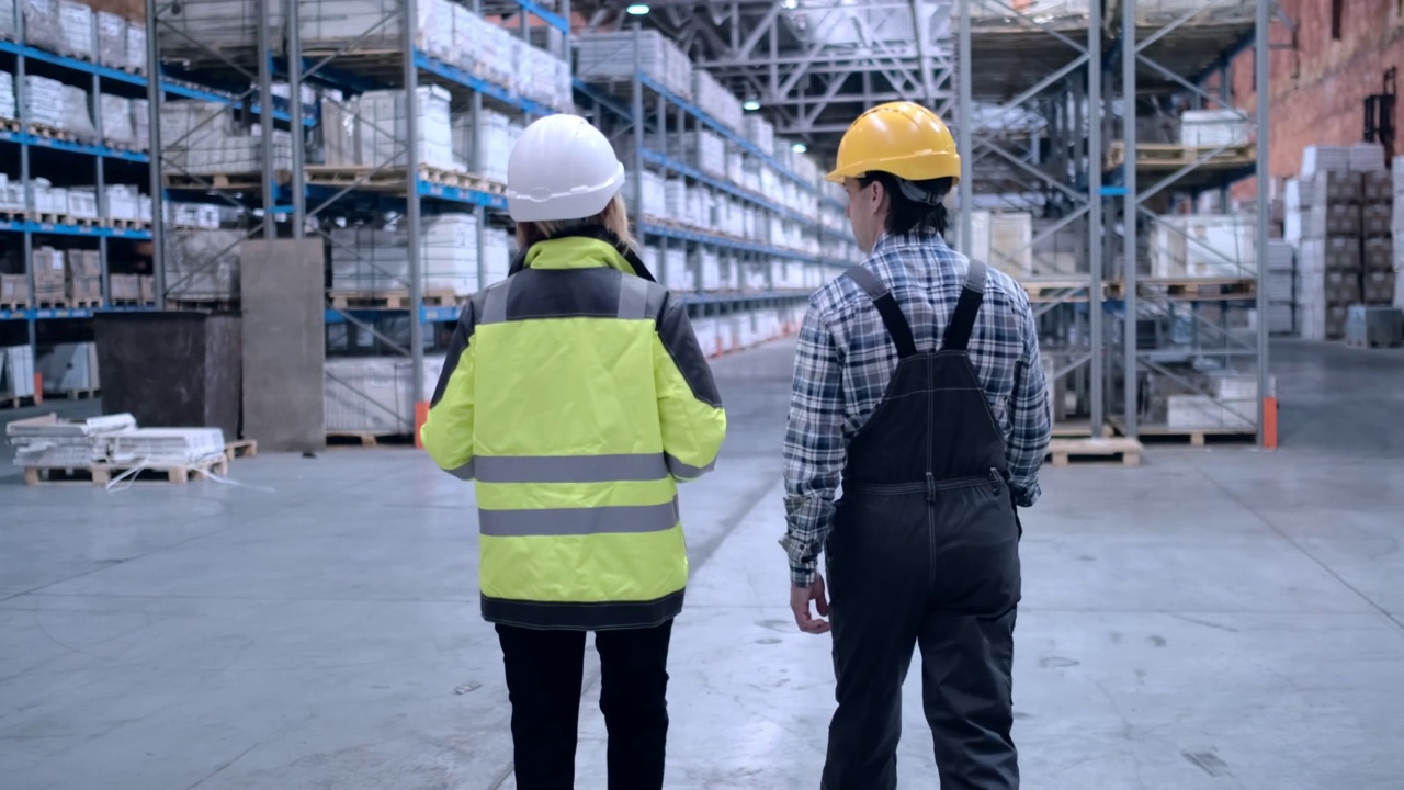 跟随员工的镜头，男性和女性仓库工人工程师在安全帽工作。走过物流中心仓库工厂建设工地物流建筑师商人建设者室内视频下载