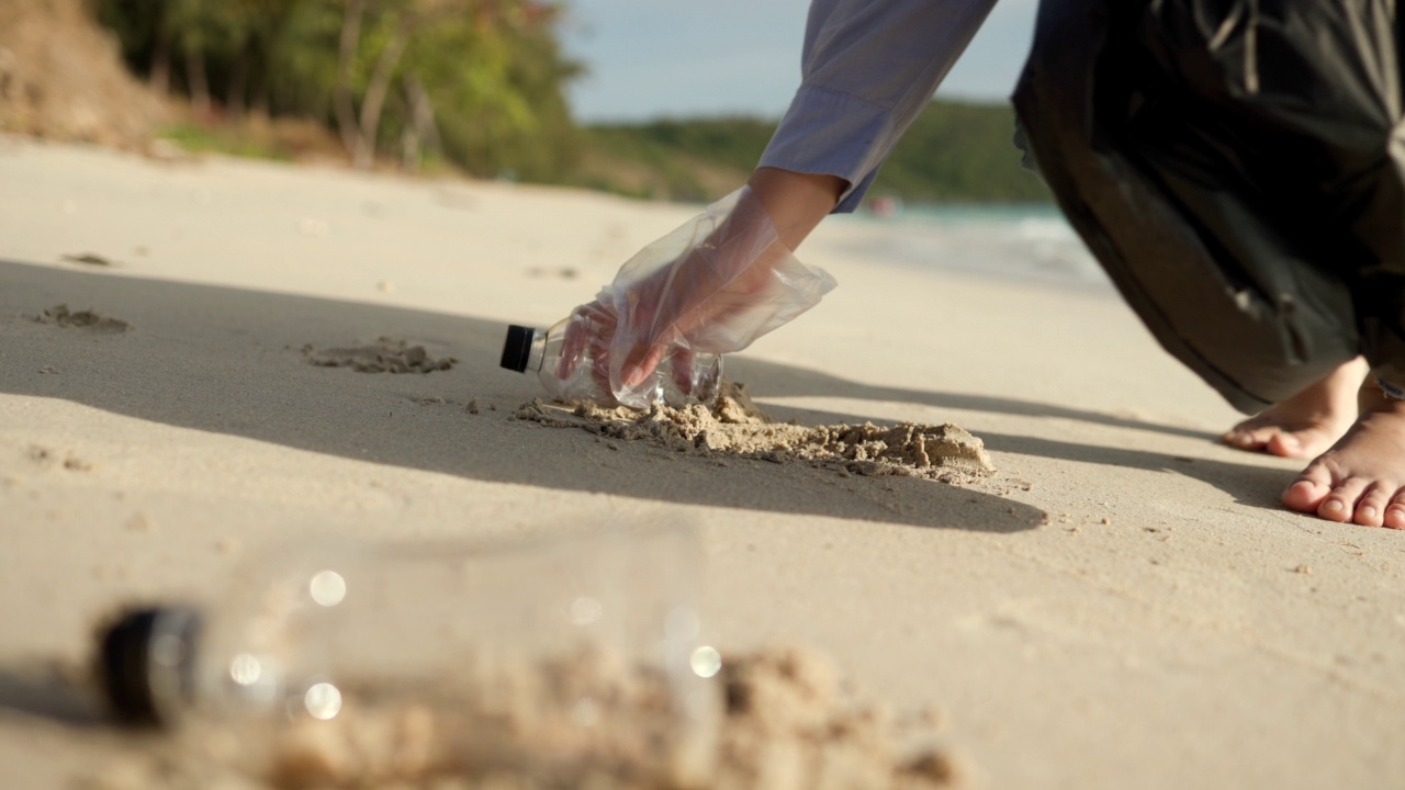 近距离拍摄，女子手捡起沙滩上的塑料瓶。女志愿者在沙滩上清理垃圾，让大海变得美丽。世界环境日的概念。拯救世界。视频素材