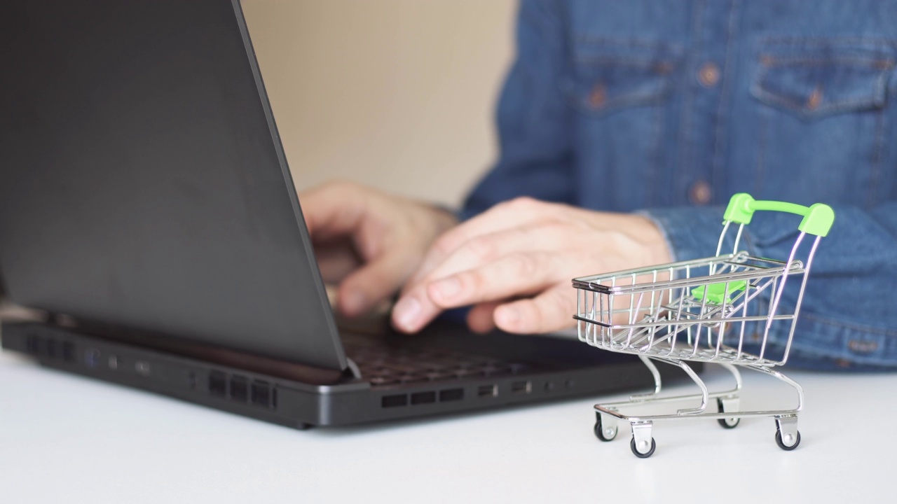 近的男人的手使用笔记本电脑进行网上支付与购物车在桌子上。网上购物的概念。视频素材