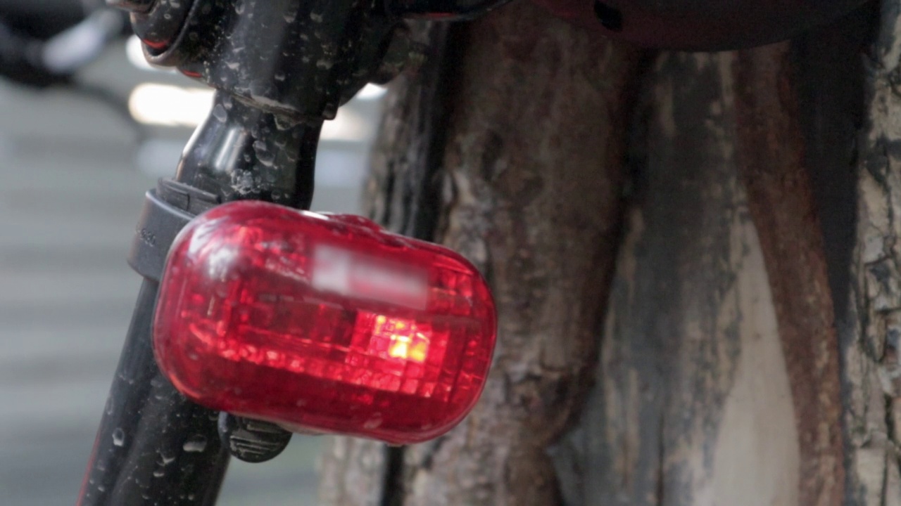 自行车红色LED闪烁尾灯。一辆停在树旁闪着红灯的自行车后面的镜头。自行车闪光器在行动视频素材