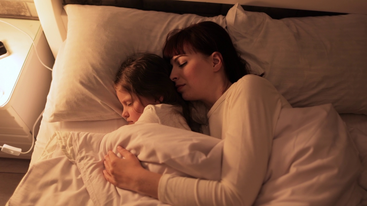 妈妈抱着可爱的女儿，一起睡在舒适的卧室里视频素材