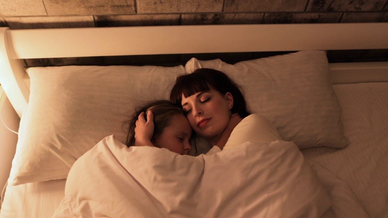 小女孩和她漂亮的妈妈躺在枕头上，拥抱着，一起睡在床上视频素材