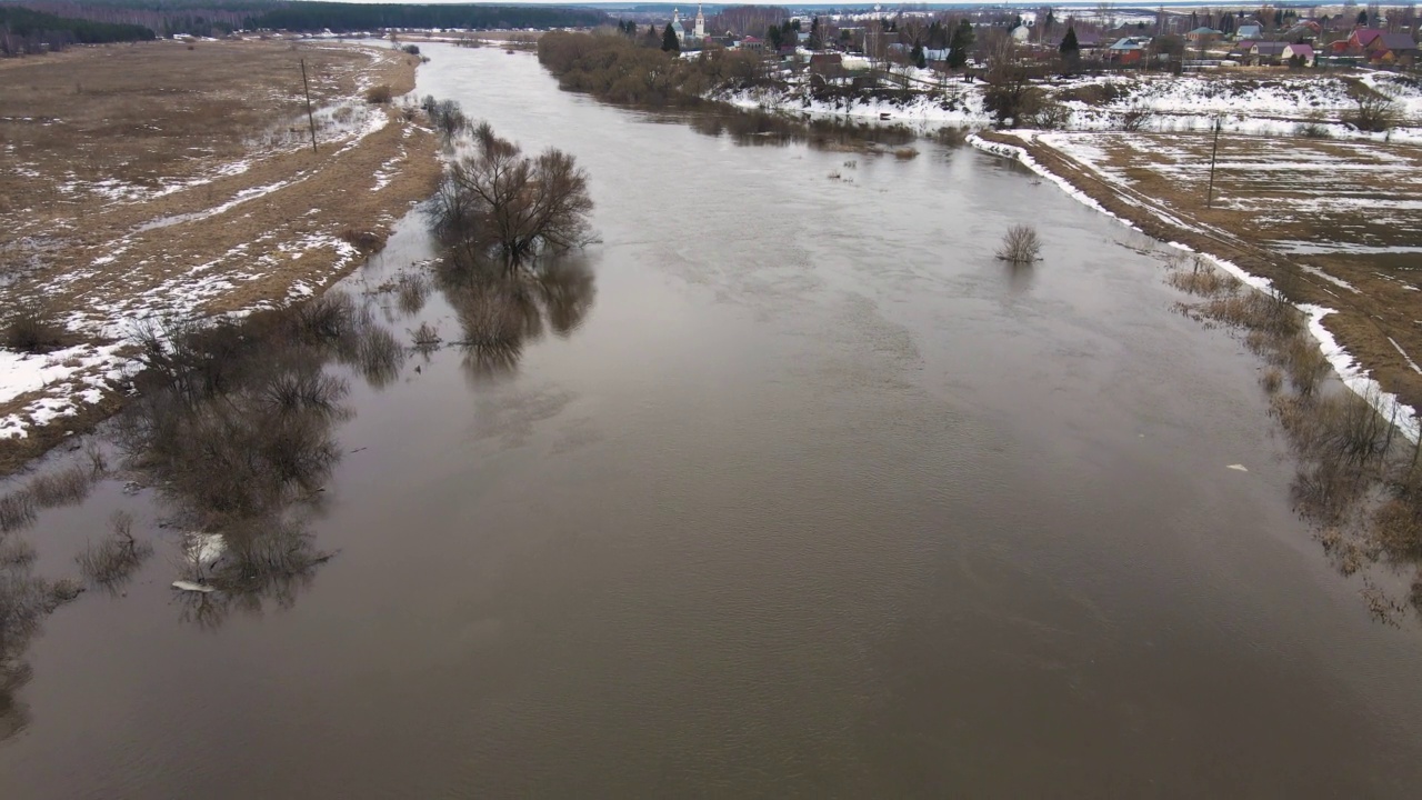 一条河流，河水浑浊灰暗，河岸上还有残存的雪堆。视频素材