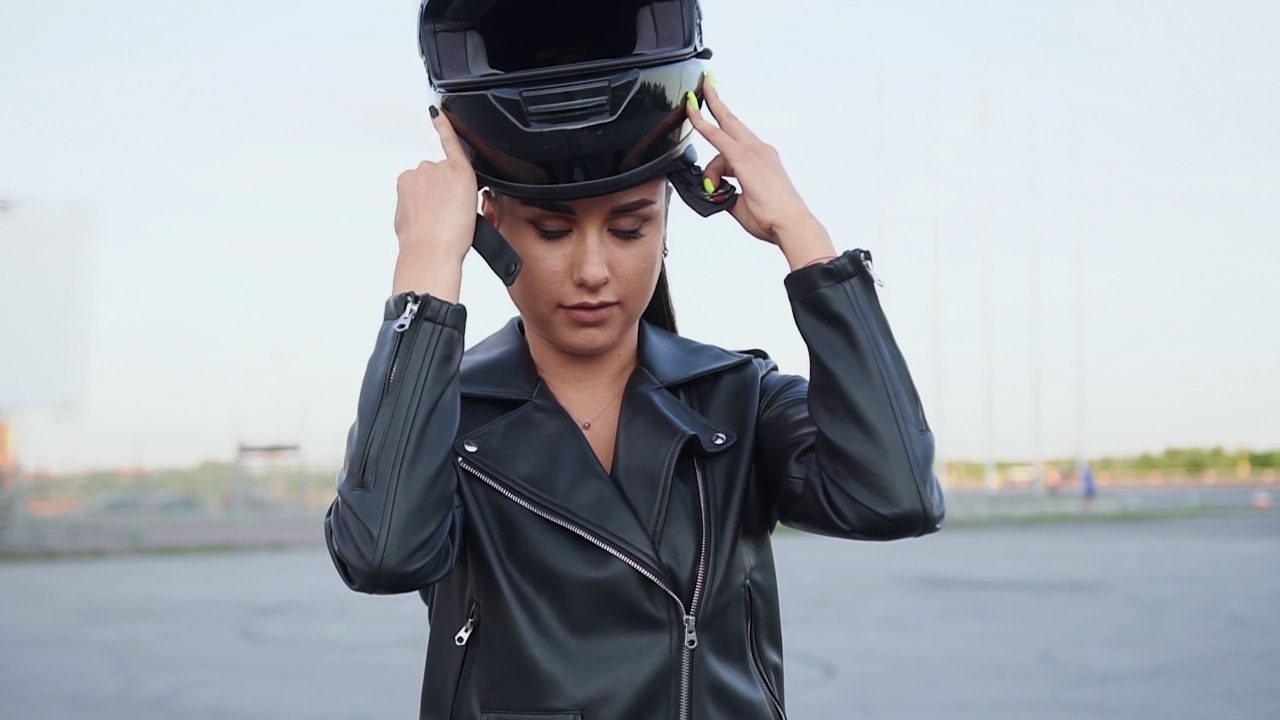 有吸引力的自信时尚的年轻女骑手戴上黑色的头盔，坐在黑色的摩托车上，看着镜头，近距离视频下载