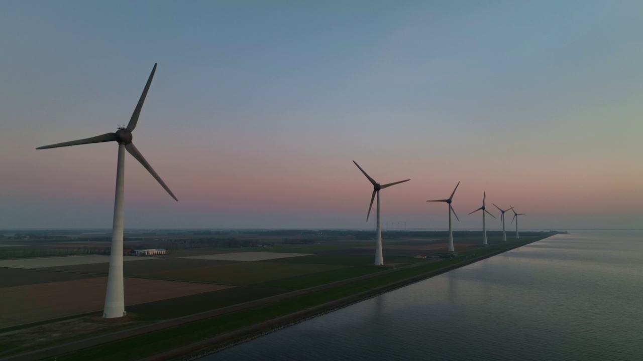 沿着湖岸的堤坝上的风力涡轮机在日落时产生可持续的可再生能源。无人机视角。视频素材