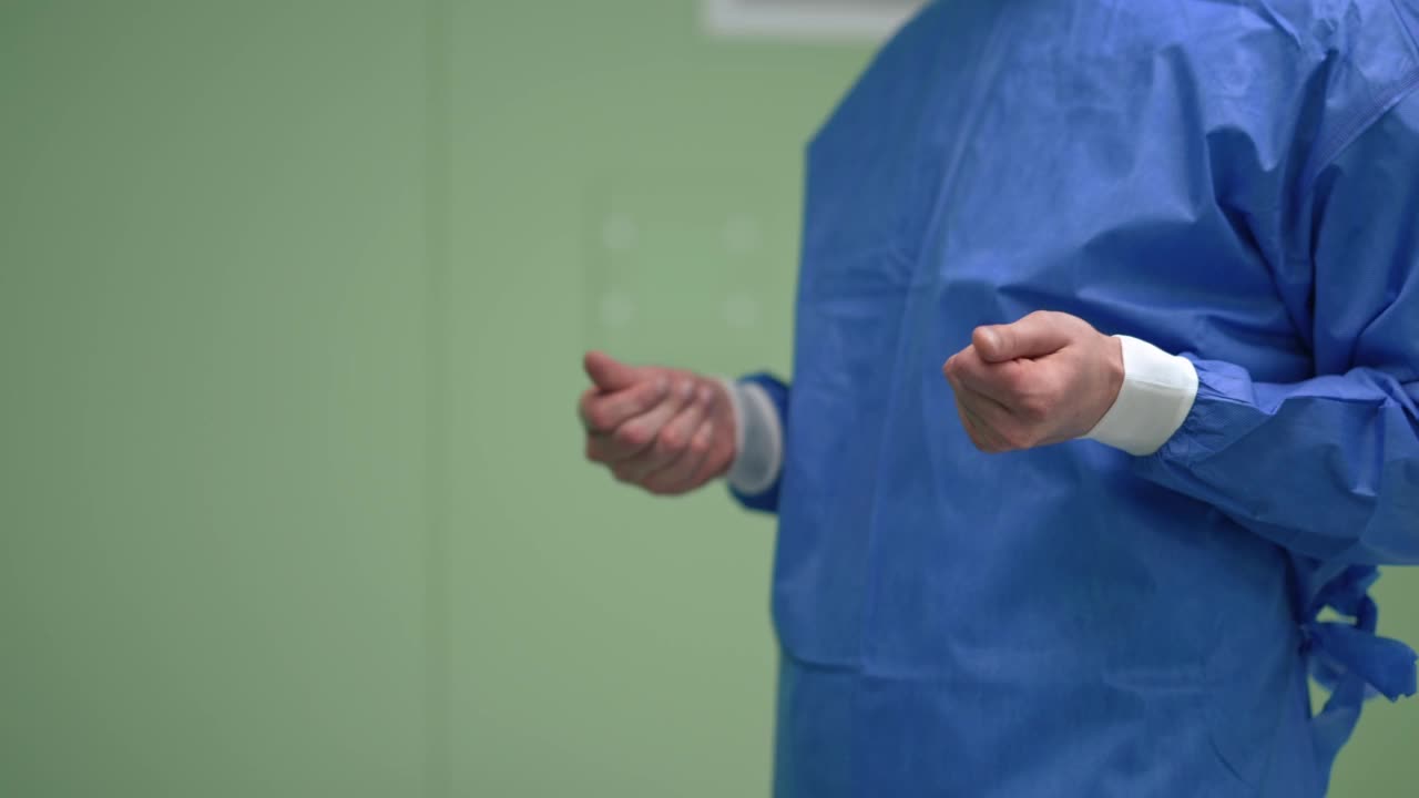 在手术室里，一名身穿手术服的白人男子在慢镜头中搓着手，站在右边。专业的专家外科医生准备在室内进行侵入性手术。视频素材