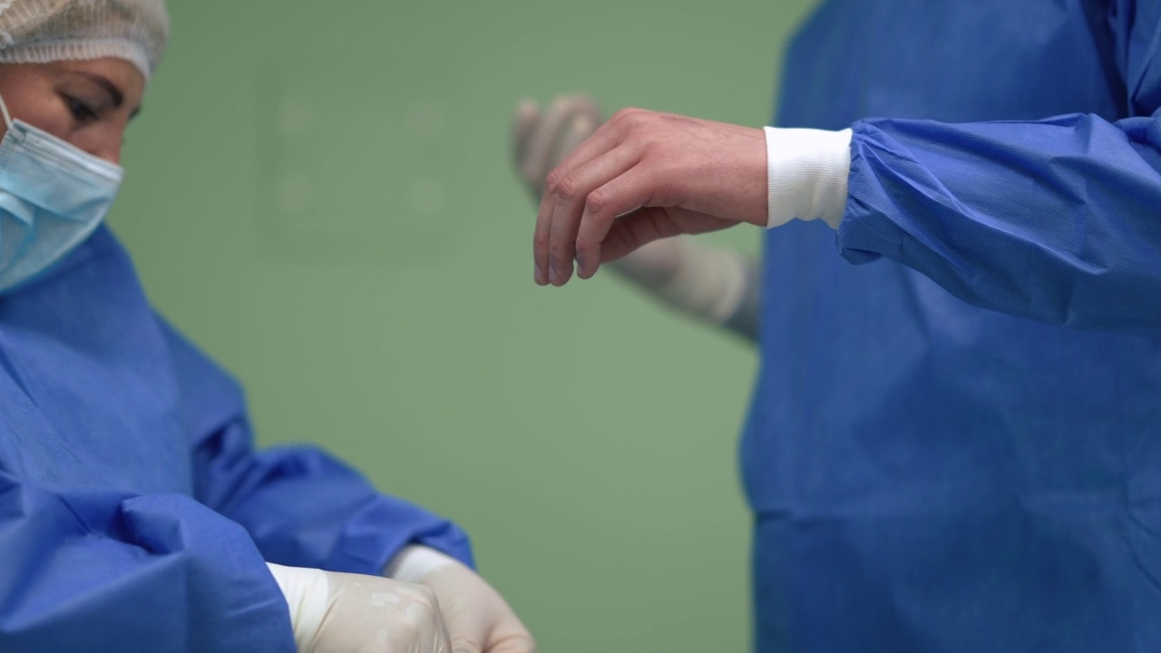 辨认不出的护士戴上手术手套，用慢镜头拍下外科医生的手。协助医生在医院室内手术室进行手术。视频下载