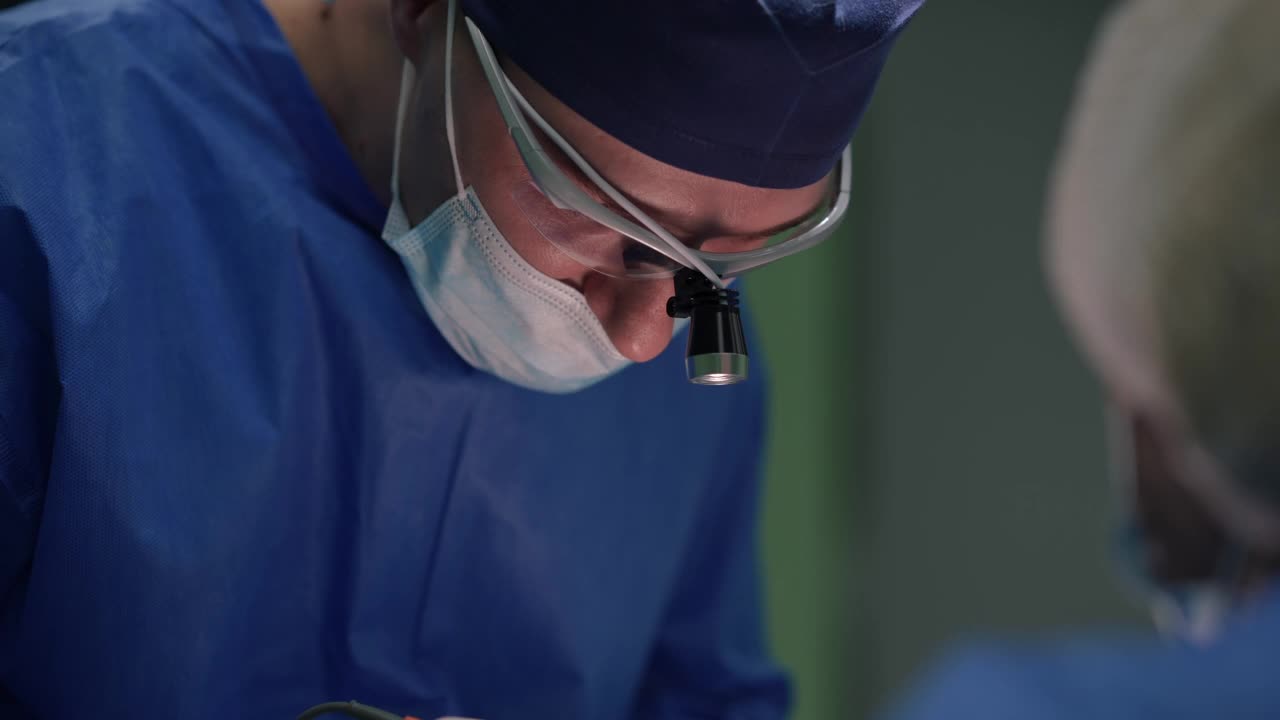白人外科专家用烧灼机缝合解剖进行眼睑成形术的肖像。在医院室内，一名自信的男子与做手术的护士助理交谈。视频素材