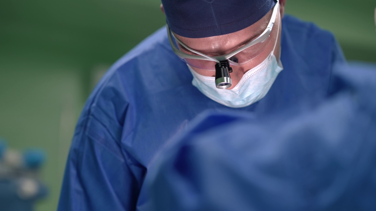 聚焦白人外科医生手术病人的前视肖像慢动作向下看。专业医生和助理在手术室协助工作。视频素材