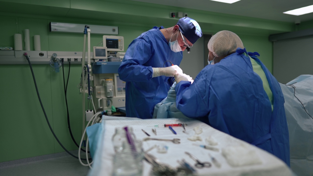 集中外科医生和护士在手术室操作病人，桌子模糊，器械在前面。白人医生和助理在医院慢镜头工作。视频素材
