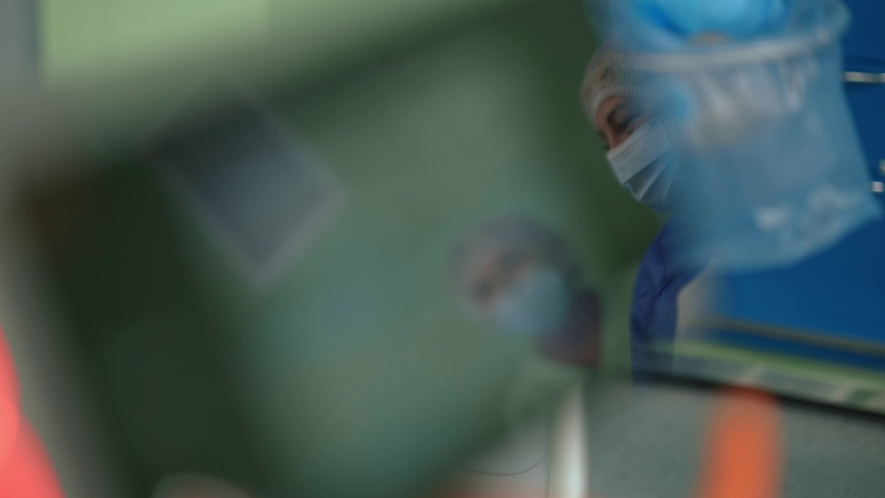 戴着外科口罩的白人护士在室内手术室的设备中反映。在医院工作的穿着制服的专业女性在侵入性手术前交谈。职业的概念。视频素材