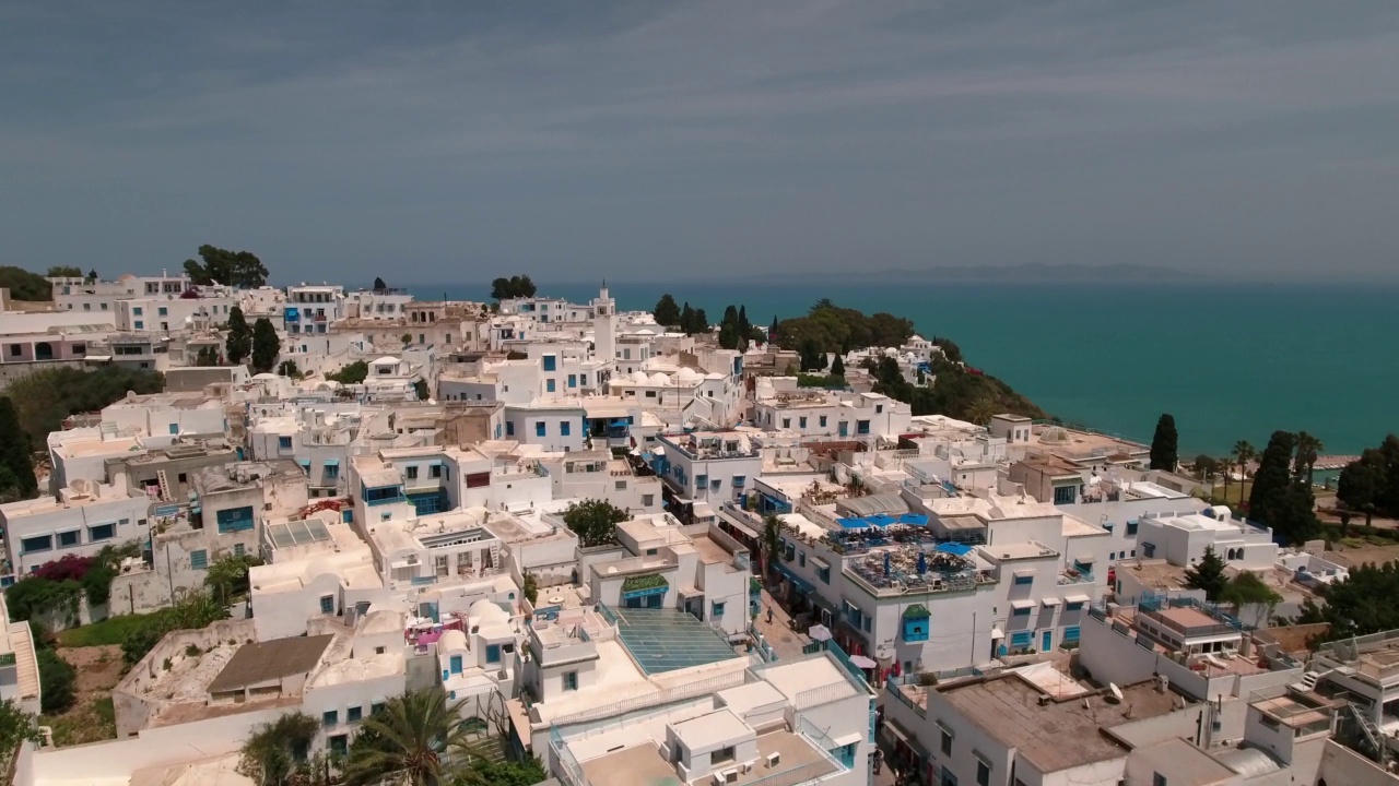 空中向前拍摄的白色住宅建筑和清真寺在镇上山上的海边-杰尔巴，突尼斯视频素材