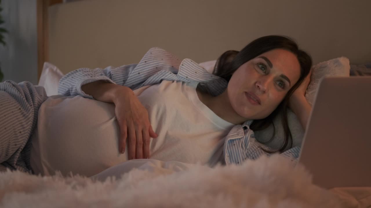 孕妇躺在床上用笔记本电脑视频聊天视频素材