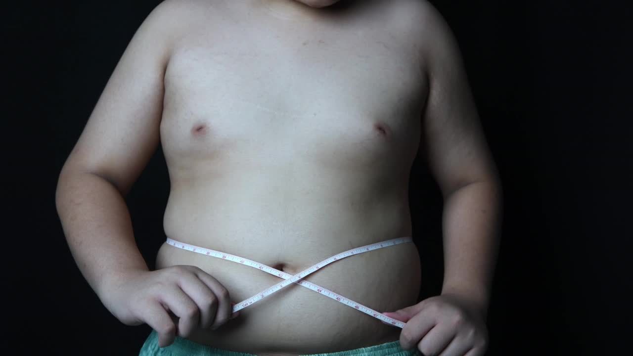 肥胖男孩用黑色背景的卷尺测量他的胖肚子，健康保健和减肥食品的概念视频素材