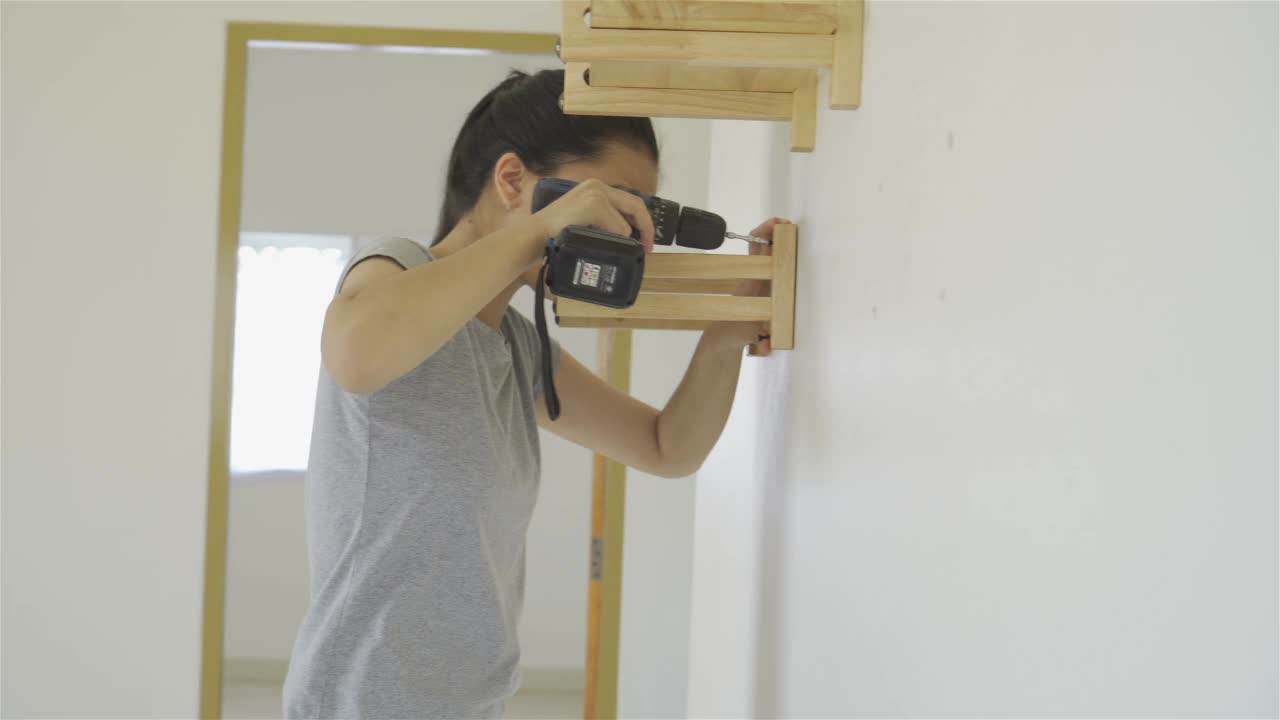 一个女人正在房子的墙上安装一个木架。视频下载