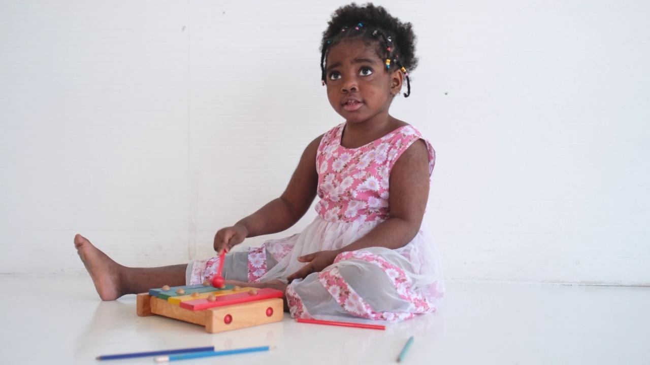 非洲裔美国女孩玩木琴作为玩具，她看起来有趣和快乐的房间的白色背景视频素材