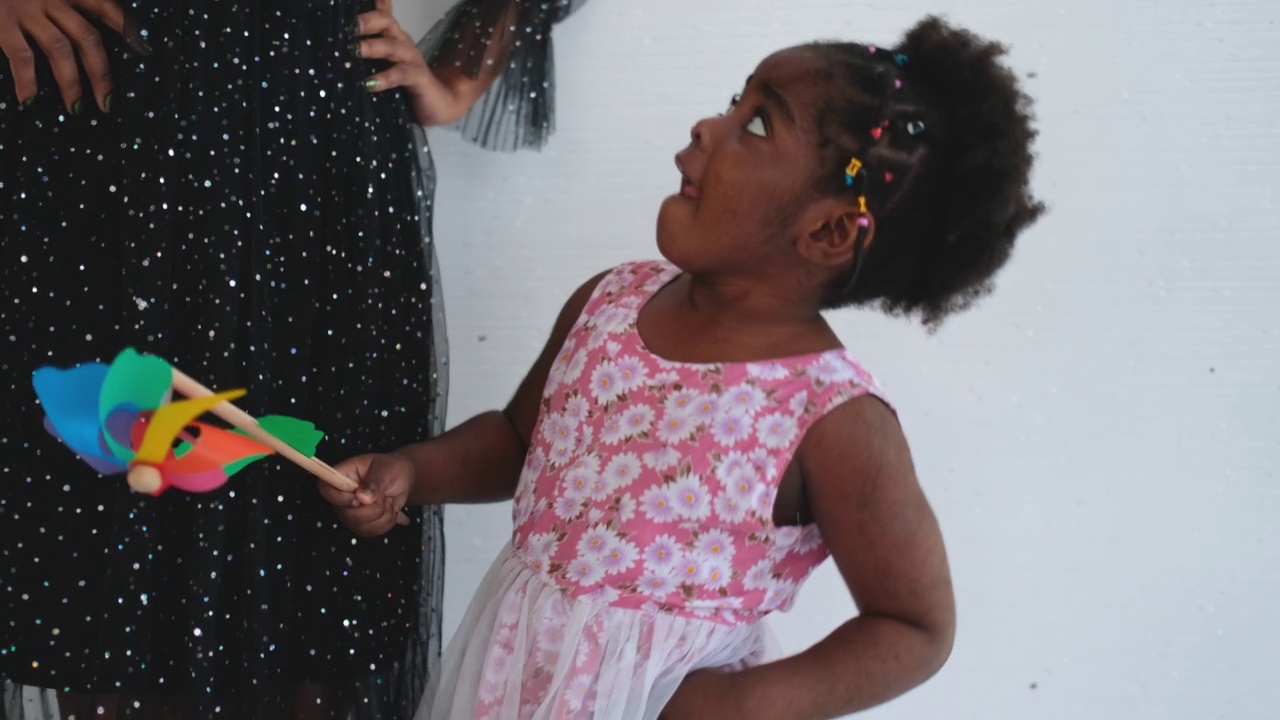 非裔美国女孩抱着风车玩具，在母亲身边快乐地跳舞视频素材