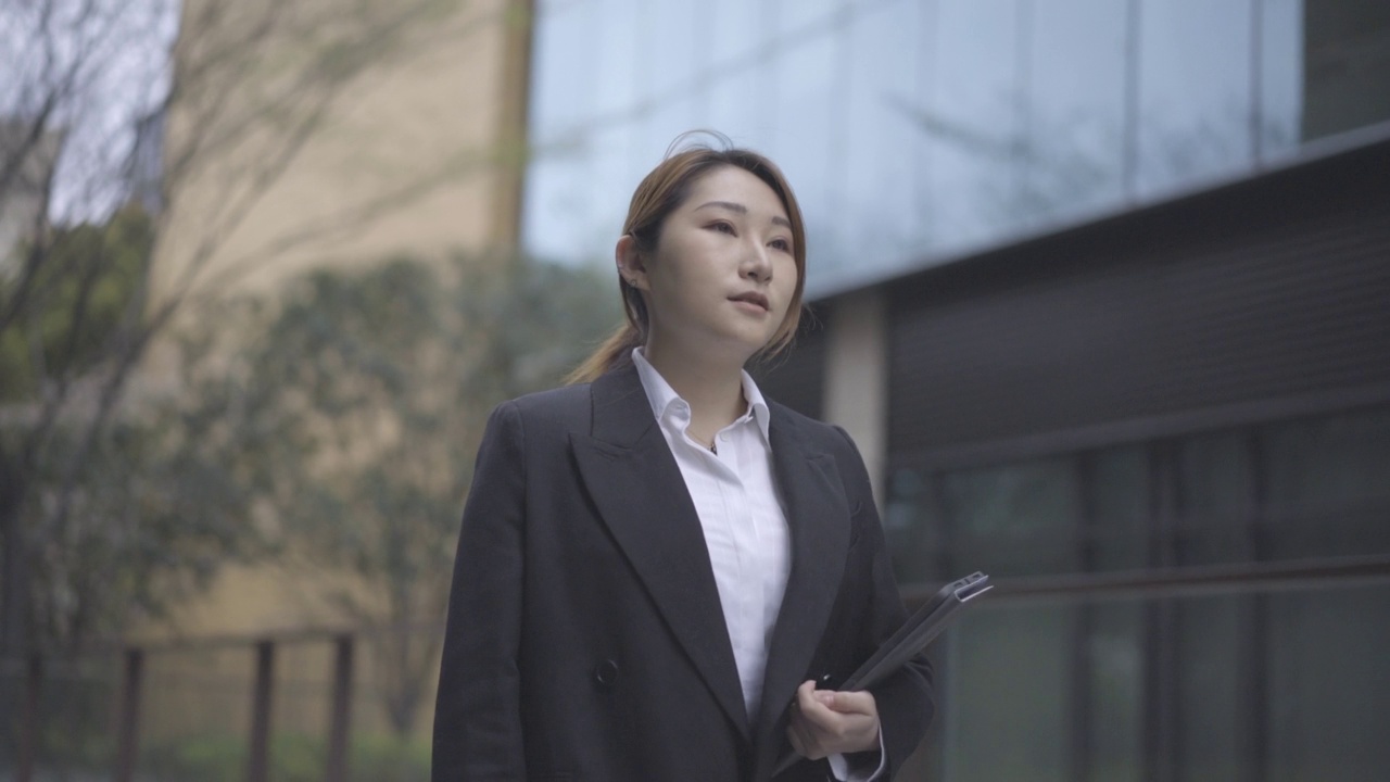 低角度拍摄的现代亚洲年轻女性在办公大楼下散步和微笑，积极和专业的性格视频素材