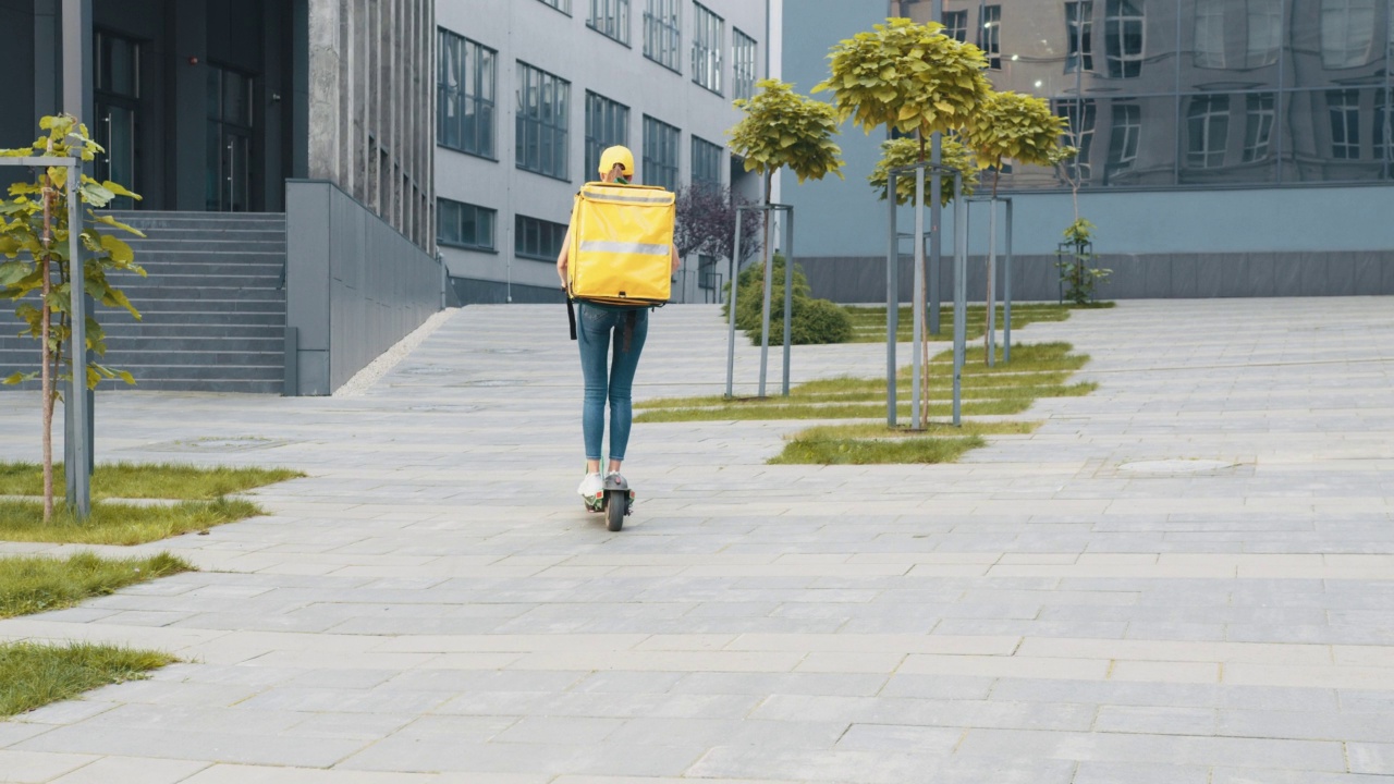 送外卖的男子背着黄色保暖背包骑着电动滑板车在街上送外卖在线订购客户客户。优秀的交付。交付货物生态运输视频素材