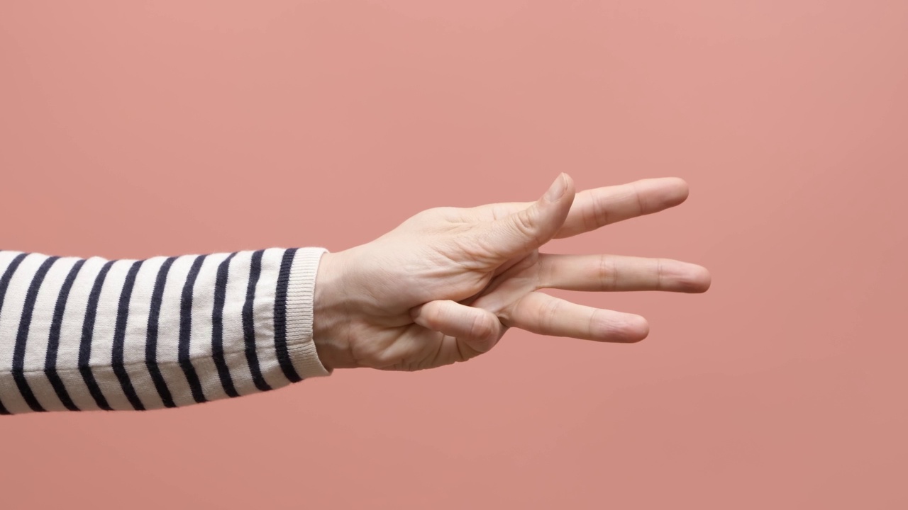 女性用手在粉色背景上从0数到5。女人展示拳头，然后一，二，三，四，五个手指，弯曲手指，从五数到一。关闭了。4 k的视频视频素材