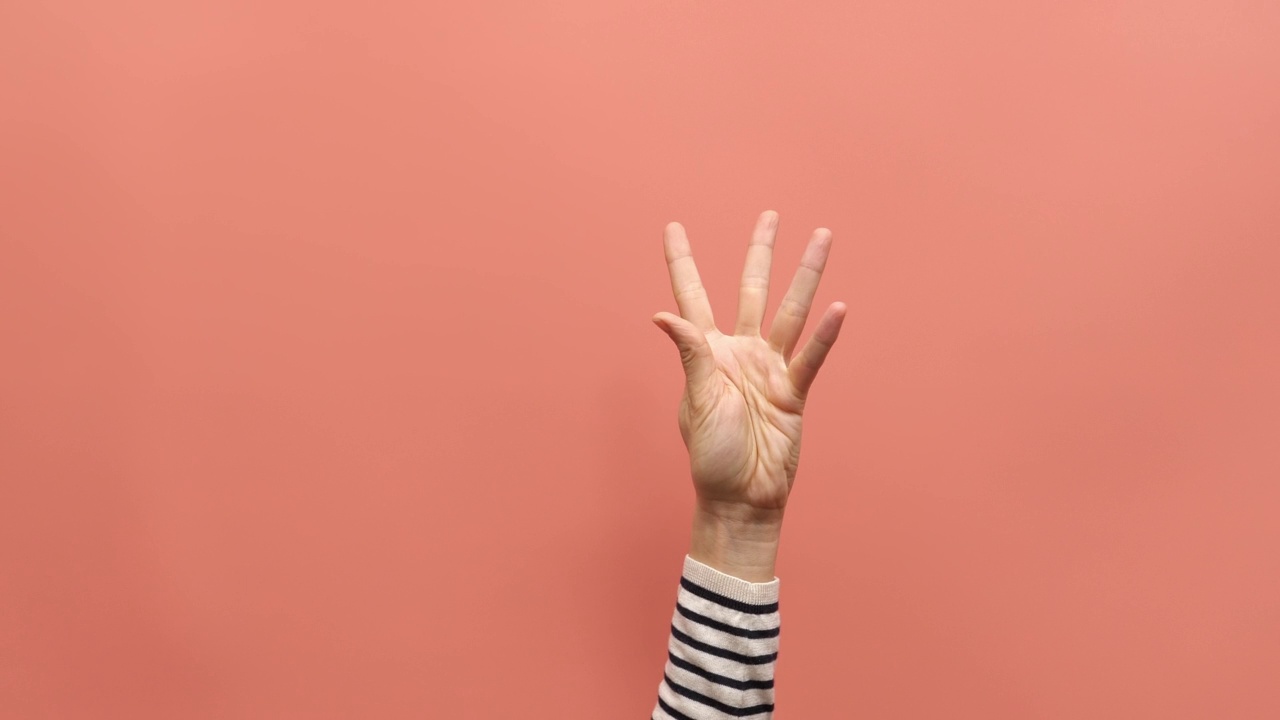 女性举手，在粉红色的背景下从0到5数数。女子展示了一，二，三，四，五个手指和弯曲的手指，从五数到一。关闭了。4 k的视频视频素材
