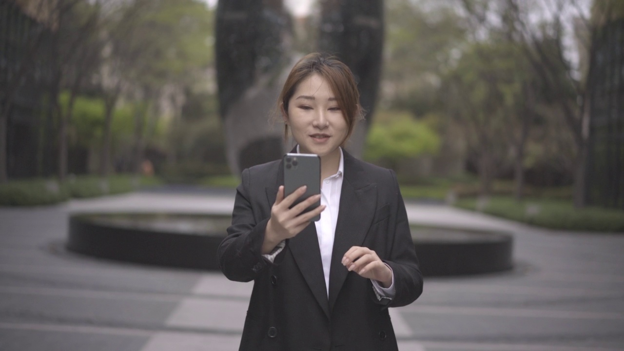 现代亚洲年轻女性在办公大楼下用智能手机工作的水平角度拍摄，美丽而专业视频素材