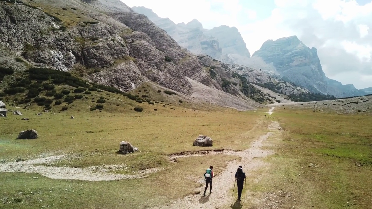 一对夫妇沿着一条穿过意大利白云石山谷的砾石小路徒步旅行。四周是高耸的山峰。石头和原始的景观。偏僻荒凉的地方自由的探索视频素材