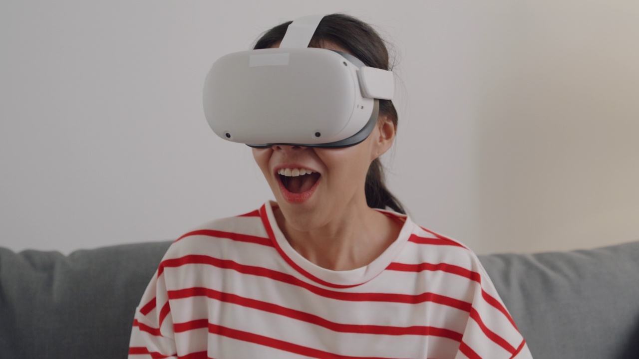 年轻女性佩戴VR头显，在家中客厅体验模拟数字世界。视频素材