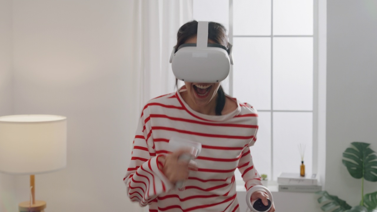 年轻女性戴上VR头戴式耳机，在家中客厅体验模拟数字世界跑步游戏动作模拟器游戏手机app。视频下载