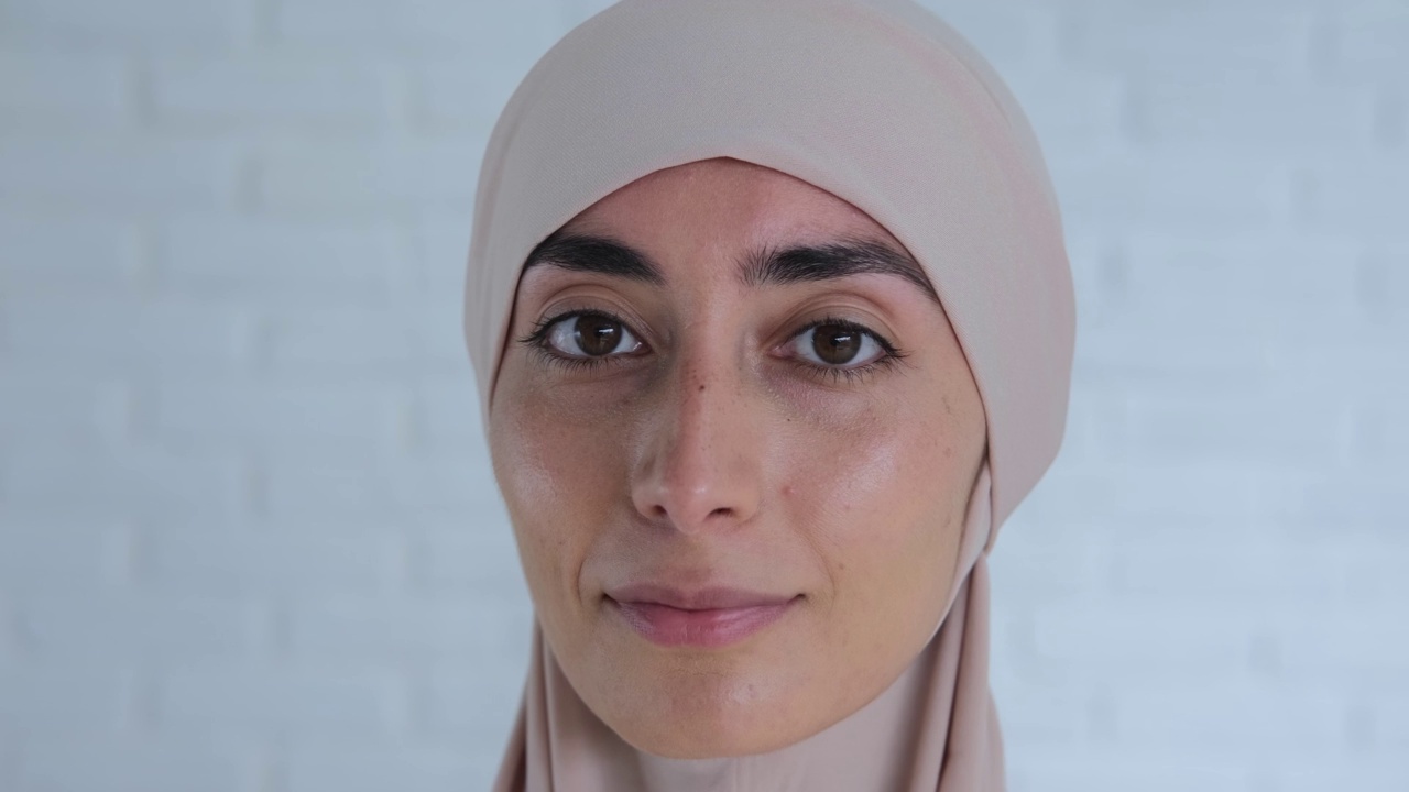 快乐微笑的阿拉伯年轻女士在希贾布头巾，开朗迷人的穆斯林妇女在摄影棚里拍摄。一个和蔼的穆斯林妇女的脸的特写，她看着相机的友好的表情视频下载