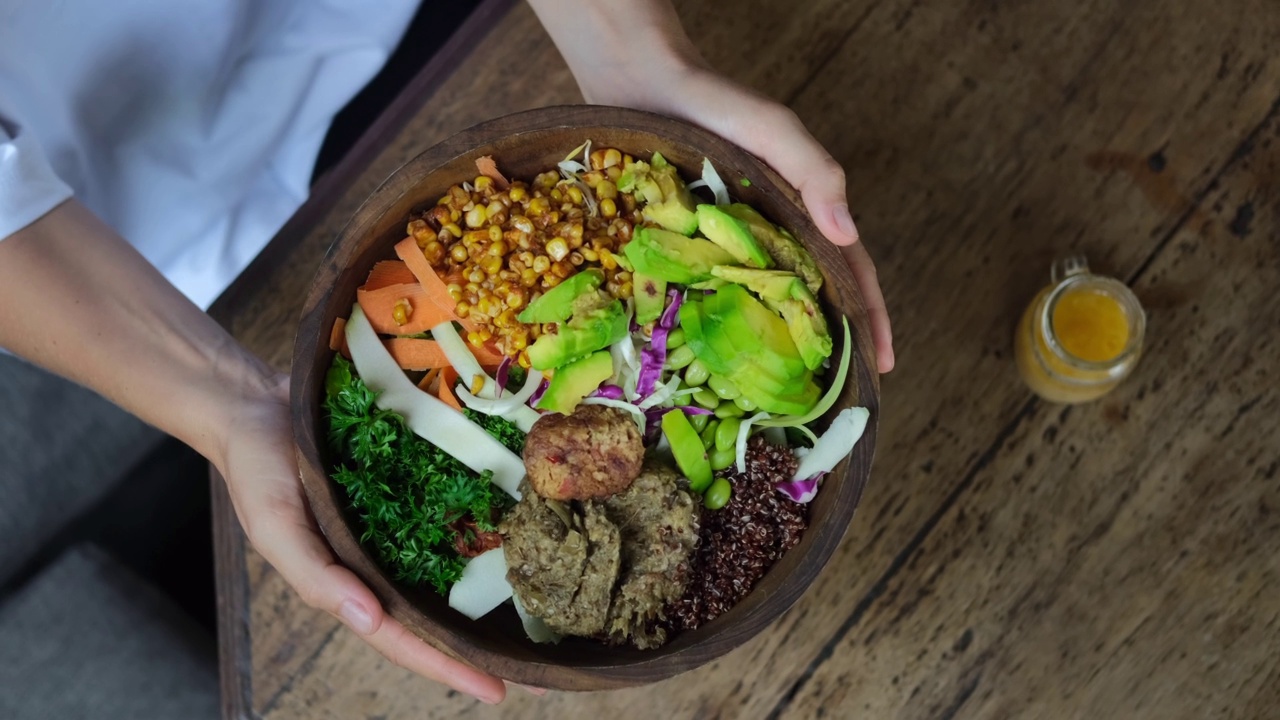 俯视图的女性手桌子设置，持有美味的健康素食碗豆腐，藜麦和鳄梨。为素食者提供健康多样的食物，包括大量的绿色蔬菜和新鲜蔬菜视频下载