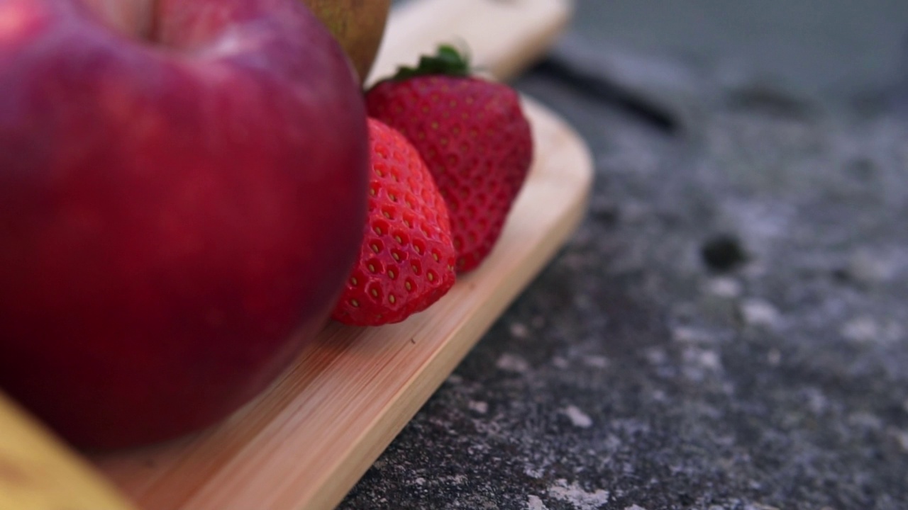 镜头移过切菜板上的美味水果。苹果，梨，香蕉，草莓。慢动作镜头。视频素材