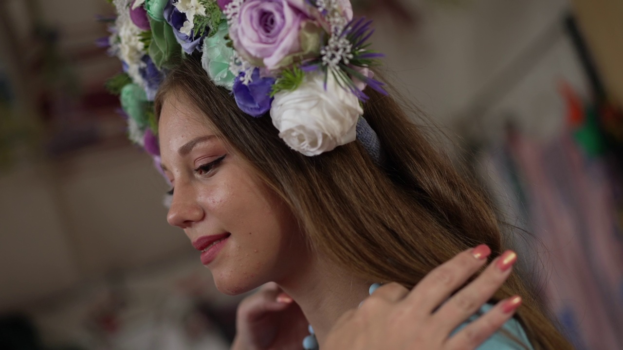 侧面特写面带微笑的乌克兰妇女，棕色的眼睛在刺绣的衣服和头环看向一边，作为女性手抚摸黑发在慢动作。女儿和母亲在室内。视频下载
