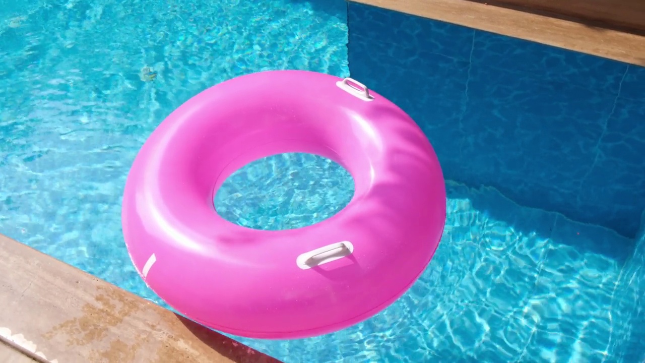 粉红色的充气环漂浮在碧水的游泳池里。旅游度假概念视频下载