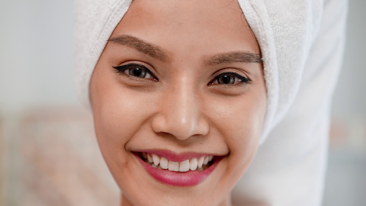 可爱微笑的年轻女子剪肖像有满意的表情戴在头上浴巾。亚洲女性在接受按摩和美体护理后，感到快乐和放松。视频下载