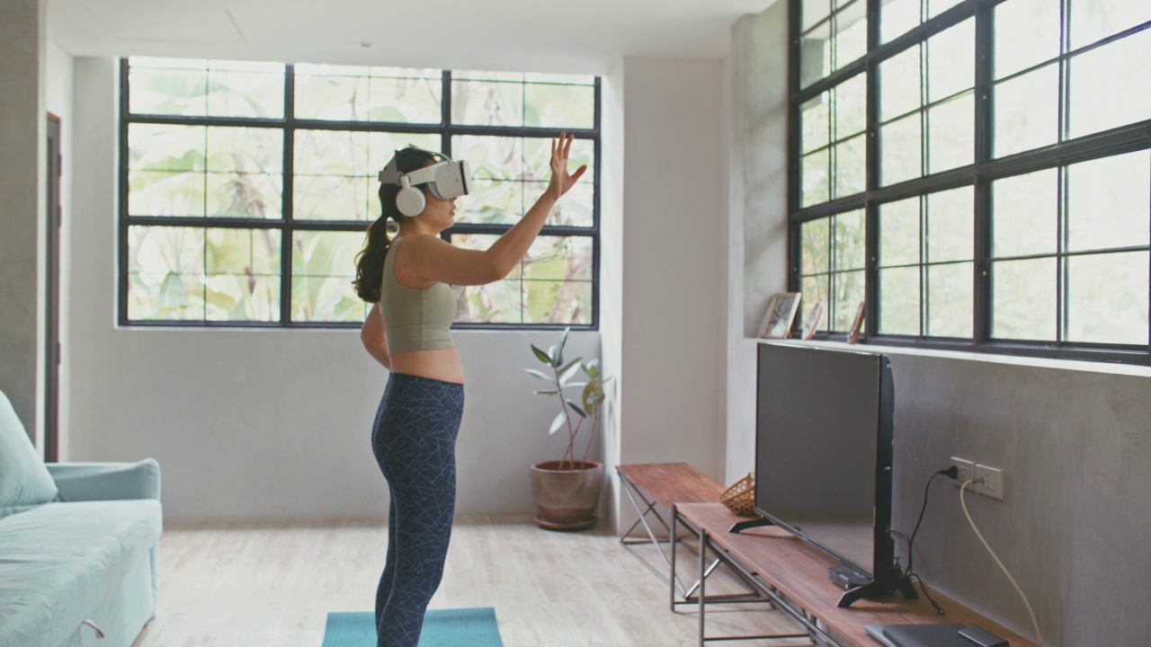 年轻的运动女性佩戴VR头盔，在家中客厅体验模拟数字世界锻炼视频素材