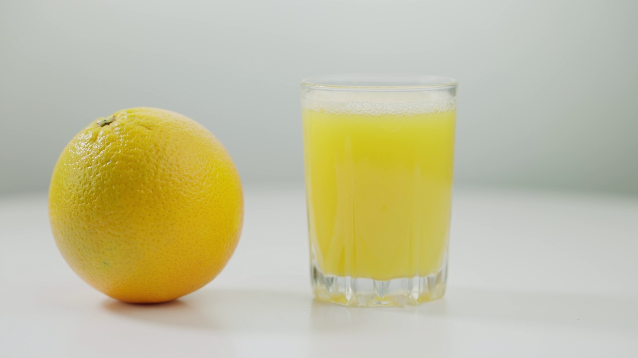 白色桌子上的橘子旋转的特写，旁边放着一杯果汁。女性的手触摸健康的维生素有机水果在白色背景。健康饮食的概念。视频素材