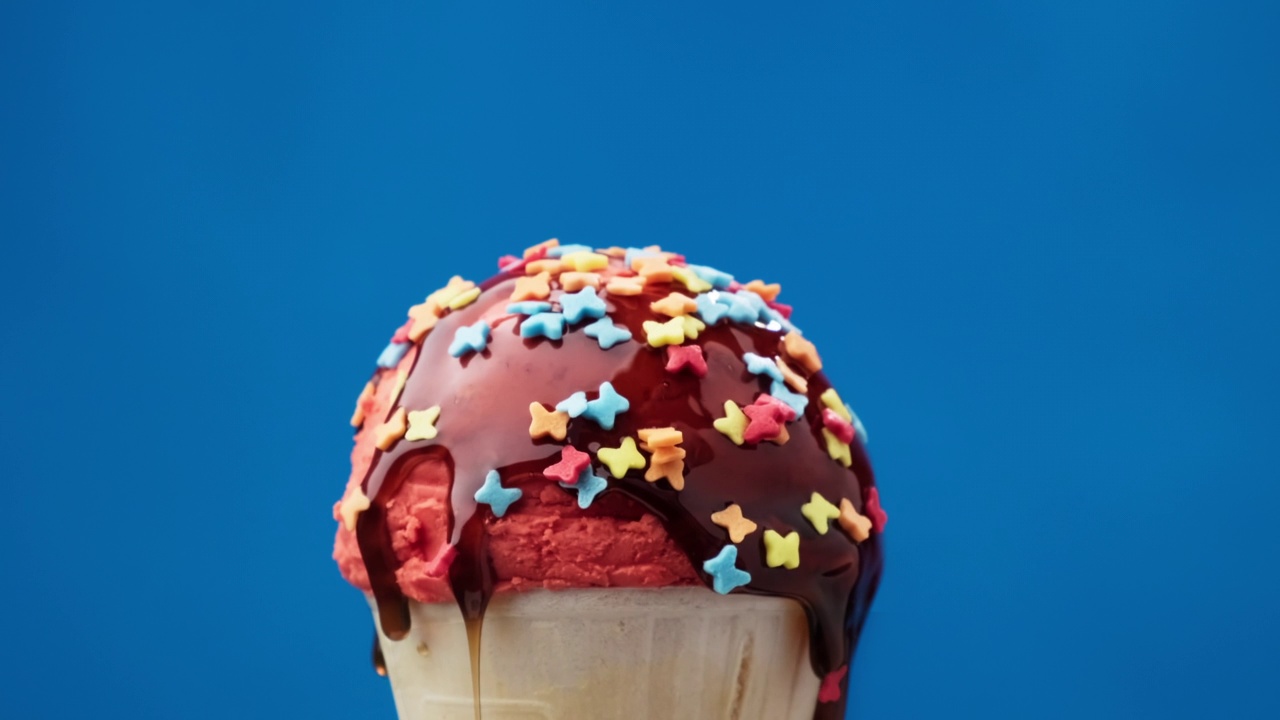 旋转草莓冰淇淋甜筒与焦糖酱蓝色背景。视频素材