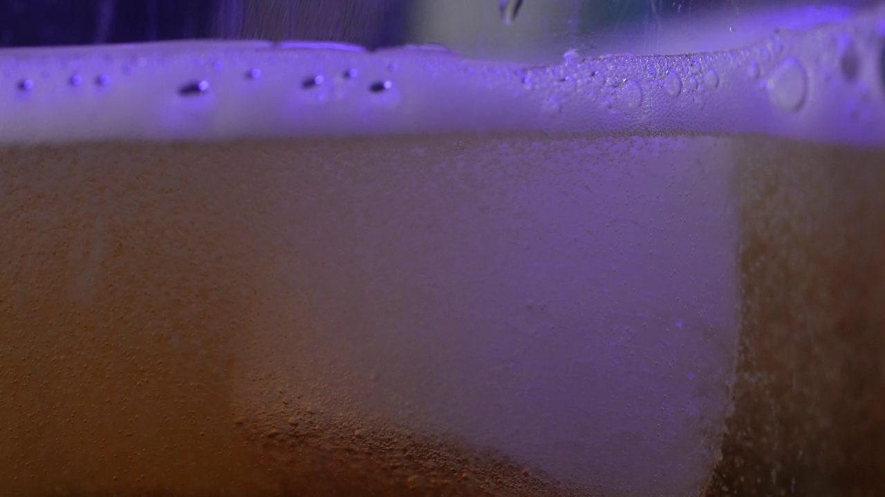 黄色啤酒的特写，宏观镜头。将啤酒与泡沫倒入玻璃中。视频下载