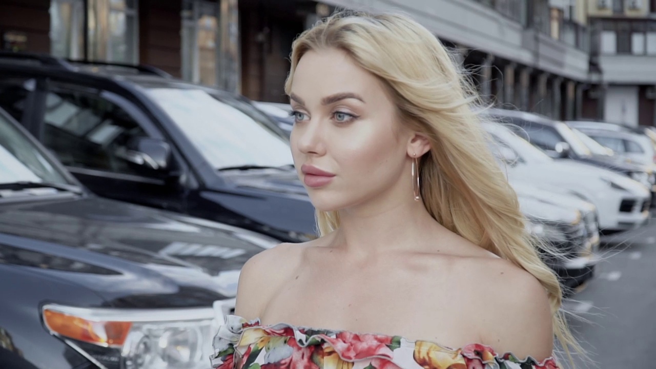 一个丰满的嘴唇和蓝眼睛的金发美女的肖像在停车场的背景上视频下载