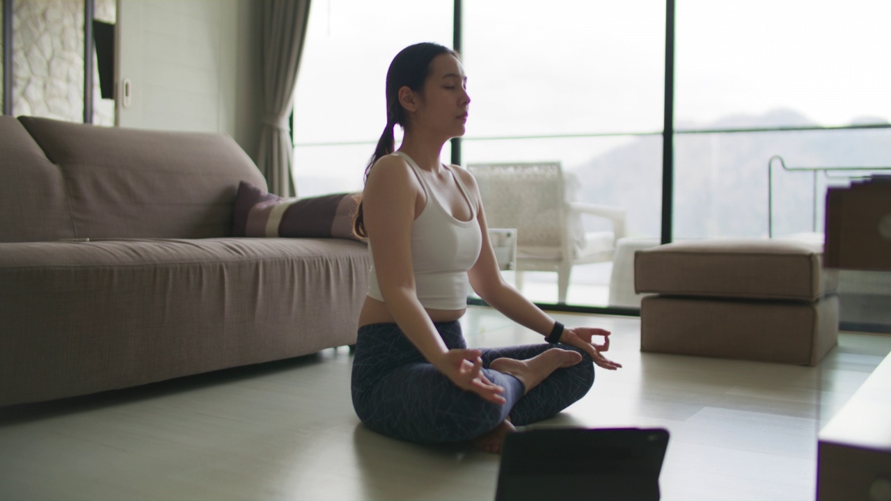 一个女人一边在笔记本电脑上看瑜伽课，一边在家做运动视频素材