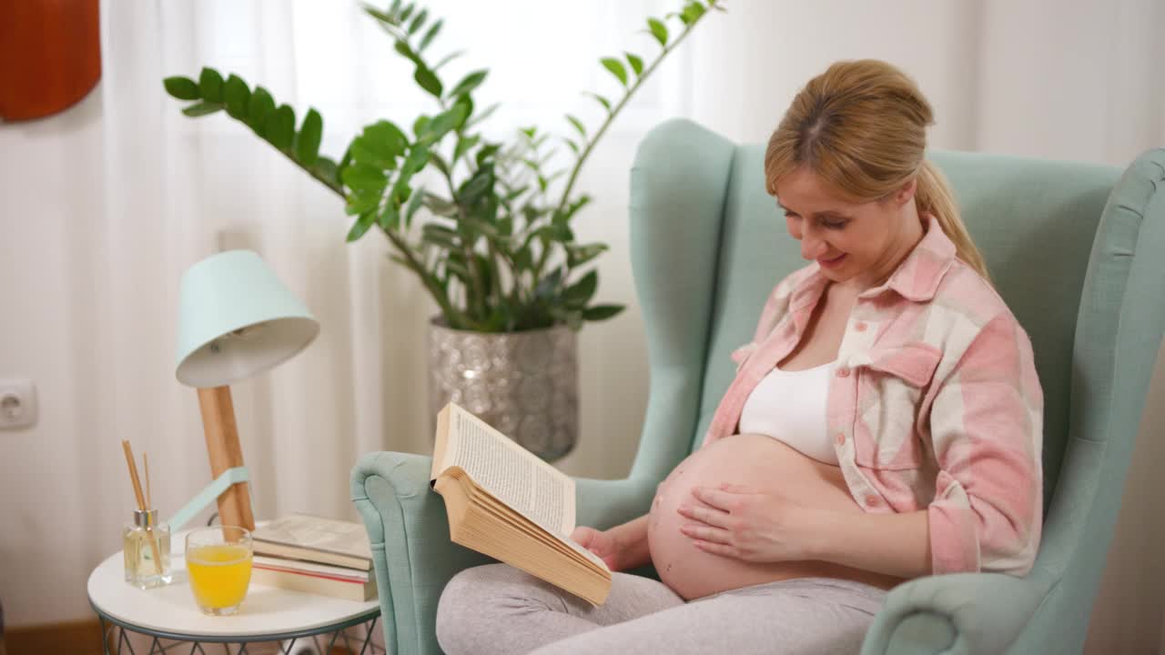 年轻的孕妇放松地坐在扶手椅上看书视频下载